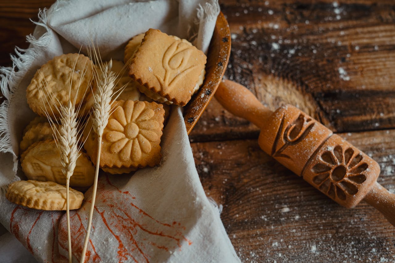 services-01 Artisan cookies with embossed designs next to a decorative rolling pin on rustic wooden surface.